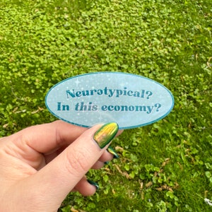 May include: A blue and white oval sticker with the text "Neurotypical? In this economy?" on a green grassy background.