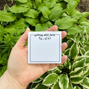 May include: White notepad with black border and the text "getting shit done" in black cursive font. The notepad has a decorative swirl design.