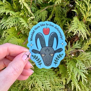 May include: A blue and white sticker with a black goat and a red apple. The sticker says "Wouldst thou like to live deliciously?"