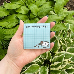 May include: A blue sticky note with a grid pattern and the text "just little guy things" in black. A cartoon illustration of a white and gray rat eating brown crumbs is at the bottom of the note.