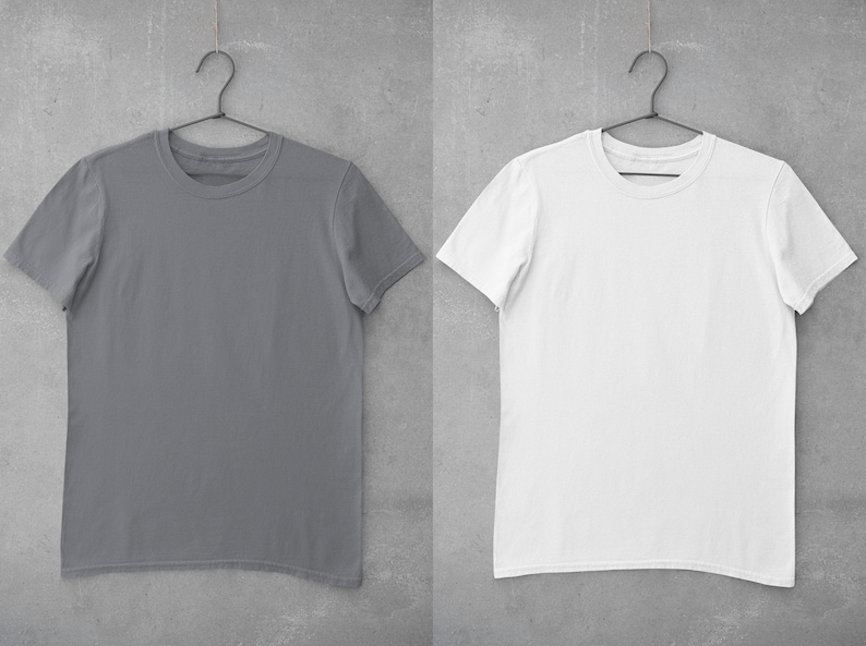 May include: Two plain t-shirts hanging on hangers against a gray concrete wall. The t-shirt on the left is gray and the t-shirt on the right is white.