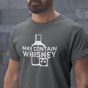 May include: A dark gray t-shirt with white text that reads "May Contain Whiskey" and a graphic of a whiskey bottle and glass.