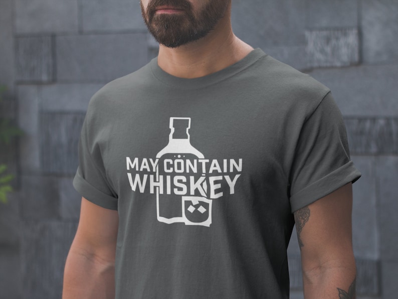 May include: A dark gray t-shirt with white text that reads "May Contain Whiskey" and a graphic of a whiskey bottle and glass.
