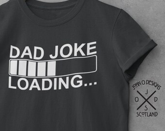 May include: A dark gray t-shirt with a white graphic that says "DAD JOKE LOADING..." with a progress bar. The shirt has a crew neck and short sleeves. The design is centered on the front of the shirt.