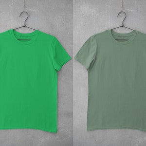 May include: Two plain t-shirts hanging on hangers against a gray concrete wall. The t-shirt on the left is bright green, and the t-shirt on the right is a muted sage green.
