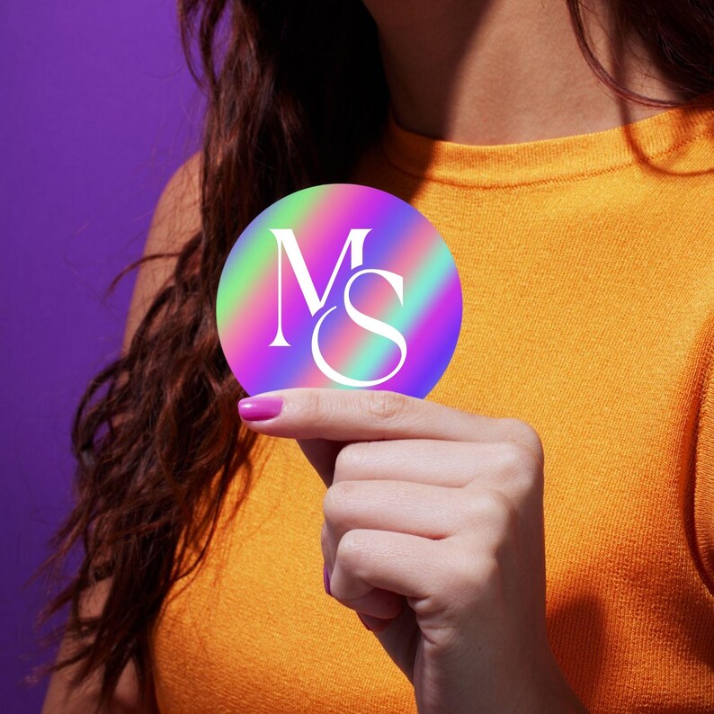 Puede incluir: Una pegatina redonda con fondo hologr&aacute;fico arco&iacute;ris y las letras "MS" en blanco.