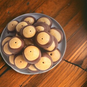 May include: A plate of chocolate-covered peanut butter candies, also known as buckeyes, arranged in a pile. The candies are a light brown color with a dark brown chocolate coating.