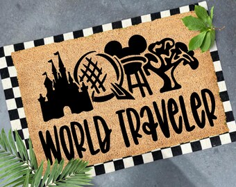 May include: Coir doormat with a black and white checkered border. The mat features black silhouettes of a castle, globe, film reel, and tree, with the words "WORLD TRAVELER" in a bold, black font.