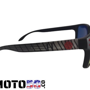 May include: Black sunglasses with a gray and white patterned frame and red accents. The lenses are yellow and blue.