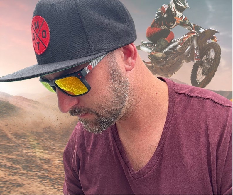 May include: A man wearing a black baseball cap with a red and white logo, yellow sunglasses, and a maroon v-neck shirt. The cap has the text "M.O.T" on it.
