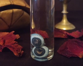 May include: A small glass bottle with a silver lid containing two blue and black eyeballs preserved in liquid.