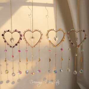 May include: Five gold heart-shaped crystal suncatchers hanging from a ceiling. Each heart is made of clear glass beads and has a smaller heart-shaped crystal hanging from the bottom. The hearts are in different colors: purple, pink, yellow, green, and blue.