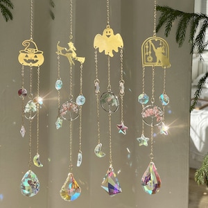 May include: Five gold-toned metal wind chimes with different Halloween-themed charms, including a pumpkin, a witch, a ghost, and a tree. Each chime features a crystal prism at the bottom and a variety of crystal beads and charms.