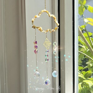 May include: A gold wire cloud-shaped crystal suncatcher with a diamond-shaped charm featuring an eye symbol. The suncatcher has three strands of crystals, each ending with a large iridescent crystal ball.