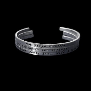 May include: A silver cuff bracelet with three bands. The bracelet has engraved text that reads "Ya Tebya Lyublyu", "I'm coming to the cottage", and "I would have loved you... Like I love". The bracelet is displayed against a black background.