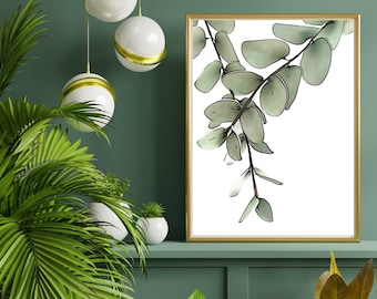 May include: A framed print of a watercolor painting of eucalyptus leaves in shades of green against a white background. The frame is gold and the print is hanging on a green wall.