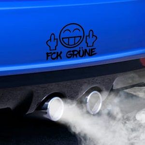 Puede incluir: Un coche azul con una pegatina negra en el parachoques trasero. La pegatina muestra una cara sonriente con dos dedos medios levantados y el texto "FCK GRÜNE". El coche está emitiendo gases de escape.