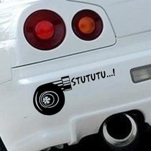 Könnte beinhalten: Ein weißes Auto mit einem schwarzen Turbolader-Aufkleber auf dem hinteren Stoßfänger. Der Aufkleber lautet "STUTUTU..."