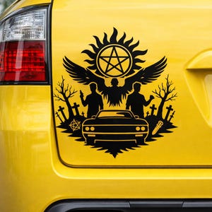 May include: Black vinyl decal featuring a stylized design with a car, figures, and symbols. The design includes a sunburst, a five-pointed star, wings, and silhouettes of people and trees. The decal is applied to a yellow car.
