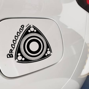 Op de afbeelding: Zwart-witte sticker van een rotatiemotor met het woord "Braaap" in een gestileerd lettertype. De sticker is aangebracht op een witte auto.