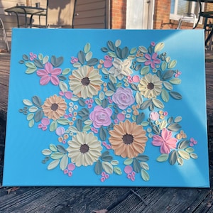 May include: A floral canvas art piece featuring a bouquet of textured flowers in shades of pink, peach, yellow, and white, with green leaves and pink berry accents, set against a bright blue background.