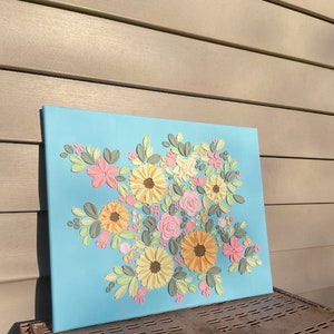 May include: A floral canvas art piece featuring a bouquet of textured flowers in shades of yellow, pink, and peach, with green and gray leaves, set against a light blue background. The artwork is displayed on a rectangular canvas.