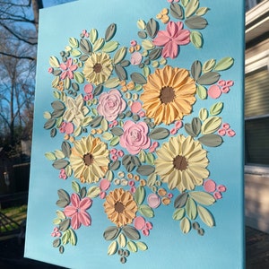 May include: A floral canvas art piece featuring textured flowers in shades of yellow, pink, and white, with green and gray leaves, set against a light blue background. The artwork is a decorative piece.