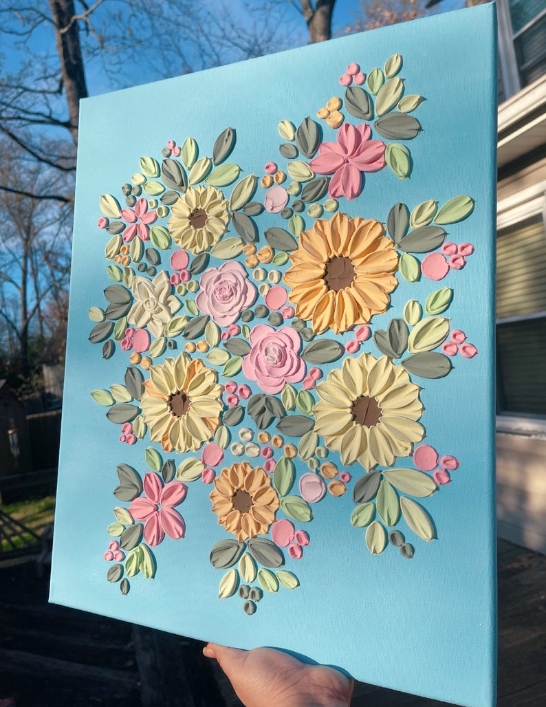 May include: A floral canvas art piece featuring textured flowers in shades of yellow, pink, and white, with green and gray leaves, set against a light blue background. The artwork is a decorative piece.