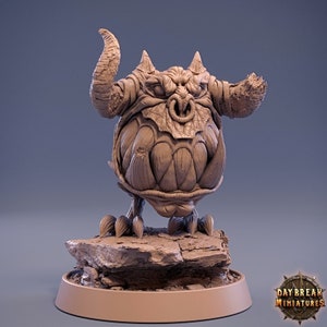 May include: A brown, sculpted miniature of a grotesque, horned creature with a large, toothy mouth. The creature is standing on a rocky base.