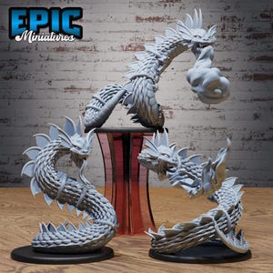 May include: Three light grey unpainted resin miniature figures of serpentine creatures with scaled bodies, fin-like crests, and open mouths. Each figure is mounted on a circular black base, with one figure elevated on a translucent red stand.