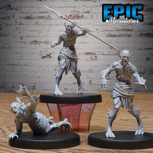 May include: Three grey unpainted miniature figures of humanoid aquatic creatures with pointed ears and fin-like appendages. One figure stands holding a long spear, another stands with arms outstretched, and the third is crouched on the ground.