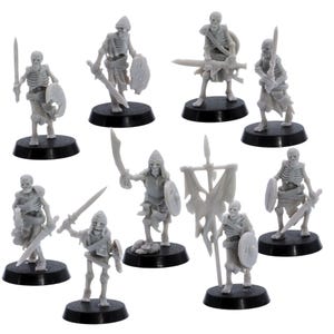 May include: A collection of miniature gray plastic skeleton figures, each posed with weapons and shields. Some skeletons hold swords, while others carry shields and banners. The figures are mounted on black circular bases, suitable for tabletop gaming or display.