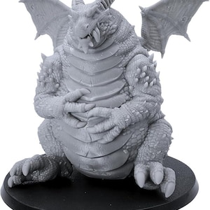 Peut inclure: Figurine de dragon gris avec des ailes, des cornes et des griffes détaillées. Le dragon est assis sur une base circulaire noire, les mains jointes. La figurine a une apparence texturée et écailleuse.