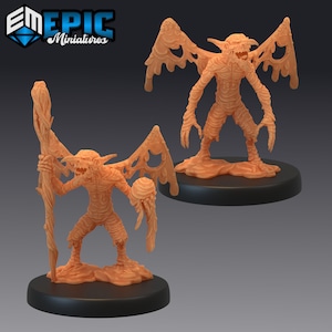 May include: Two miniature figures of grotesque, fleshy creatures with wings. The figures are painted in a light orange colour and are standing on black bases. One figure is holding a staff, while the other is holding a sphere.
