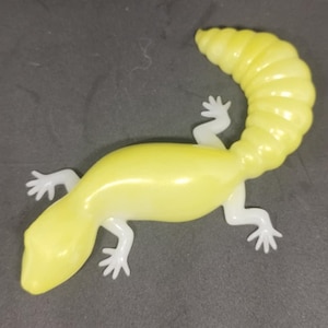 Peut inclure: Un jouet en caoutchouc jaune en forme de lézard avec une queue enroulée. Le jouet est fait d'un matériau souple et flexible et a une apparence réaliste.