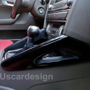 Può includere: Pezzo di rivestimento interno per auto nero lucido con leva del cambio e portabevande. Il rivestimento è installato in un'auto con sedili in pelle rossa. Il testo "Uscardesign" è visibile nell'angolo inferiore sinistro dell'immagine.