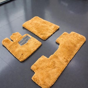 May include: A set of four tan car floor mats. The mats are made of a plush, absorbent material. One mat is rectangular, the others are custom-shaped to fit the car's interior. The mats are designed to protect the car's flooring from dirt and spills.