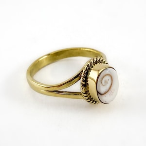 Puede incluir: Un anillo de oro con una incrustación de concha blanca. La concha tiene un patrón de espiral marrón.