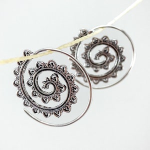 Puede incluir: Un par de pendientes de aro de plata con un diseño en espiral. Los pendientes están colgados de una cuerda.