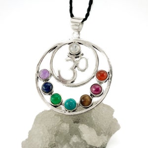 Puede incluir: Colgante de plata Om con siete piedras preciosas de chakra dispuestas en un diseño circular. Las piedras preciosas son amatista, lapislázuli, aventurina verde, turquesa, ojo de tigre, cornalina roja y rubí.
