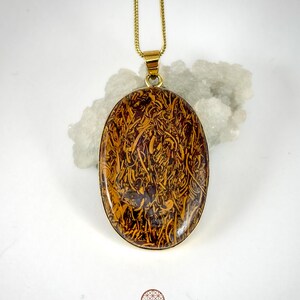 Puede incluir: Un collar de cadena dorada con un colgante ovalado con un patrón de mármol marrón y dorado.