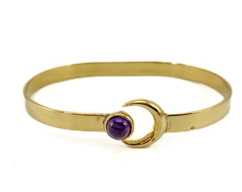 May include: A gold bangle bracelet with a crescent moon charm and a purple gemstone in the center.