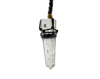 May include: A clear quartz crystal point pendant with a black cord and gold accents. The crystal is wrapped with black cord and has a pointed tip.