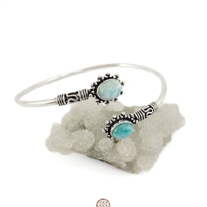 May include: A silver bangle bracelet with two oval-shaped blue gemstones set in ornate silver settings. The bracelet is open and has a delicate design.