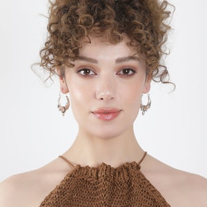 May include: A woman with curly brown hair wearing a brown halter top and silver hoop earrings.