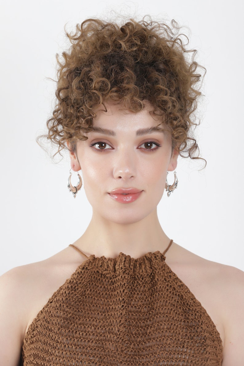 May include: A woman with curly brown hair wearing a brown halter top and silver hoop earrings.