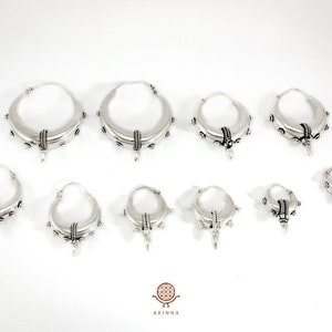 May include: Set of nine silver hoop earrings with a textured design and a pointed detail. The earrings are available in various sizes.