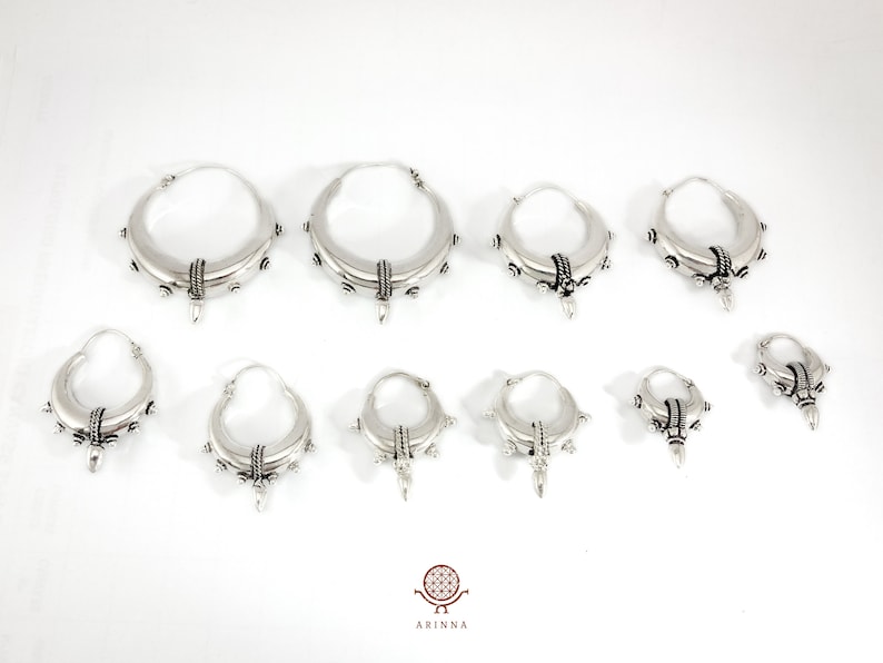 May include: Set of nine silver hoop earrings with a textured design and a pointed detail. The earrings are available in various sizes.