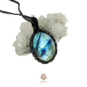 Könnte beinhalten: Ein blauer und grüner Labradorit-Edelstein-Anhänger mit einer schwarzen Schnurkette. Der Anhänger ist oval geformt und hat eine natürliche, unregelmäßige Form.