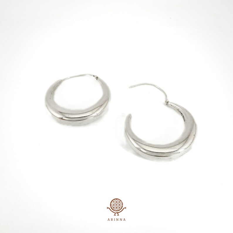 May include: A pair of silver hoop earrings with a curved, rounded shape. The earrings are simple and elegant.